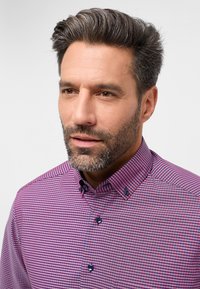 Camicia a quadri in tonalità di rosa e viola, con colletto a camicia, bottoni blu e tessuto textured. Primo piano sul collo e sul viso.
