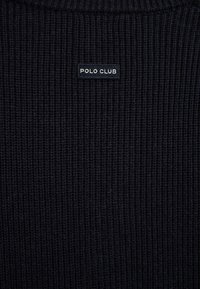 Tessuto a maglia costellata di colore blu navy scuro con una piccola etichetta rettangolare cucita sopra, con testo bianco che recita "POLO CLUB."