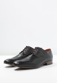 Chaussures en cuir noir à bout pointu, design à lacets avec des accents marron contrastants. Texture lisse et détails de couture minimaux.