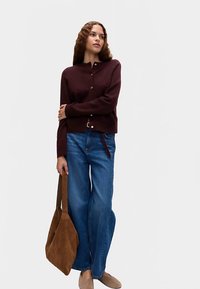 Vinröd knäppkofta, blå vida jeans, brun mockaväska och tanfärgade skor kompletterar outfiten. Minimalistisk design och mjuk textur.