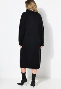 Schwarzes Strickkleid mit hohem Kragen, langen Ärmeln und gerippten Bündchen. Besitzt ein knielanges Design mit einem strukturierten Muster an den Seiten.