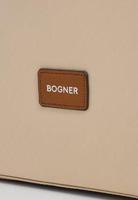Rjav usnjen pravokoten zaklop z belim napisem "BOGNER" našit na bež teksturirano tkanino.