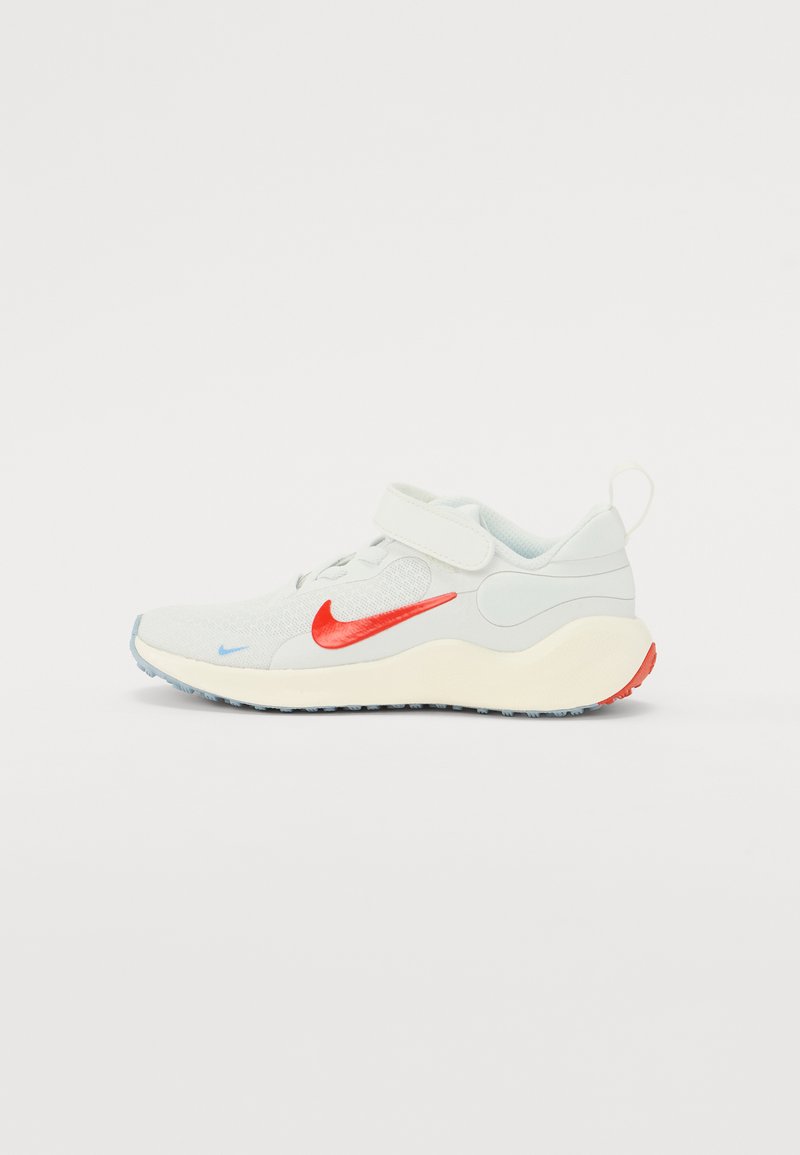 Zapatilla deportiva de color gris claro con una correa blanca, el swoosh rojo de Nike, acentos azules y una parte superior texturizada. Cuenta con una suela gruesa y acolchada.
