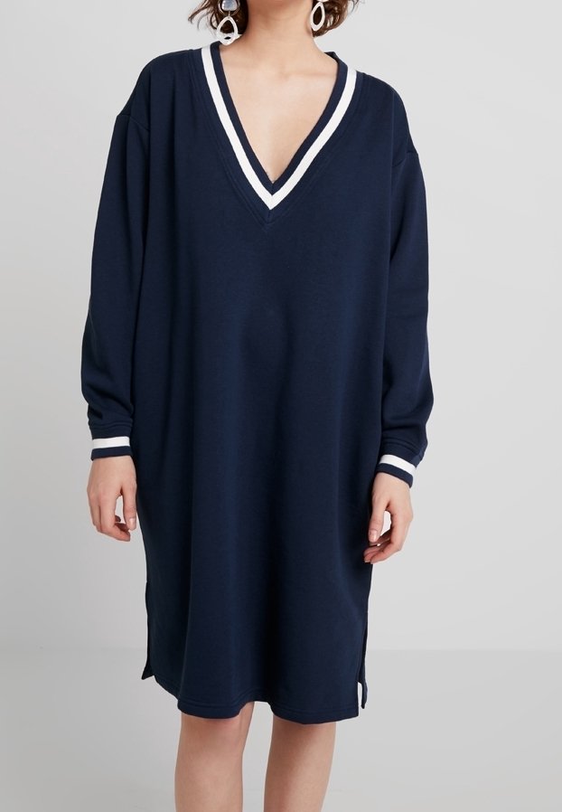 Robe oversize bleu marine en tissu doux, avec un décolleté en V profond et des rayures blanches sur le col et les manches. Fentes sur les côtés.