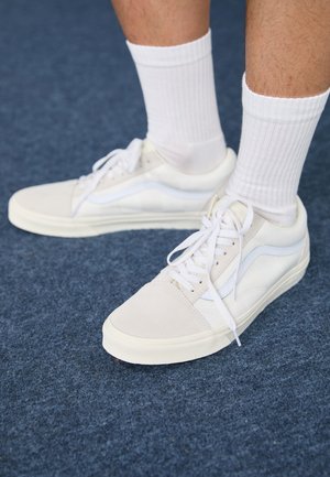 White suede sneakers with a smooth texture, featuring white laces and an accent swoosh design, paired with white ribbed socks.
