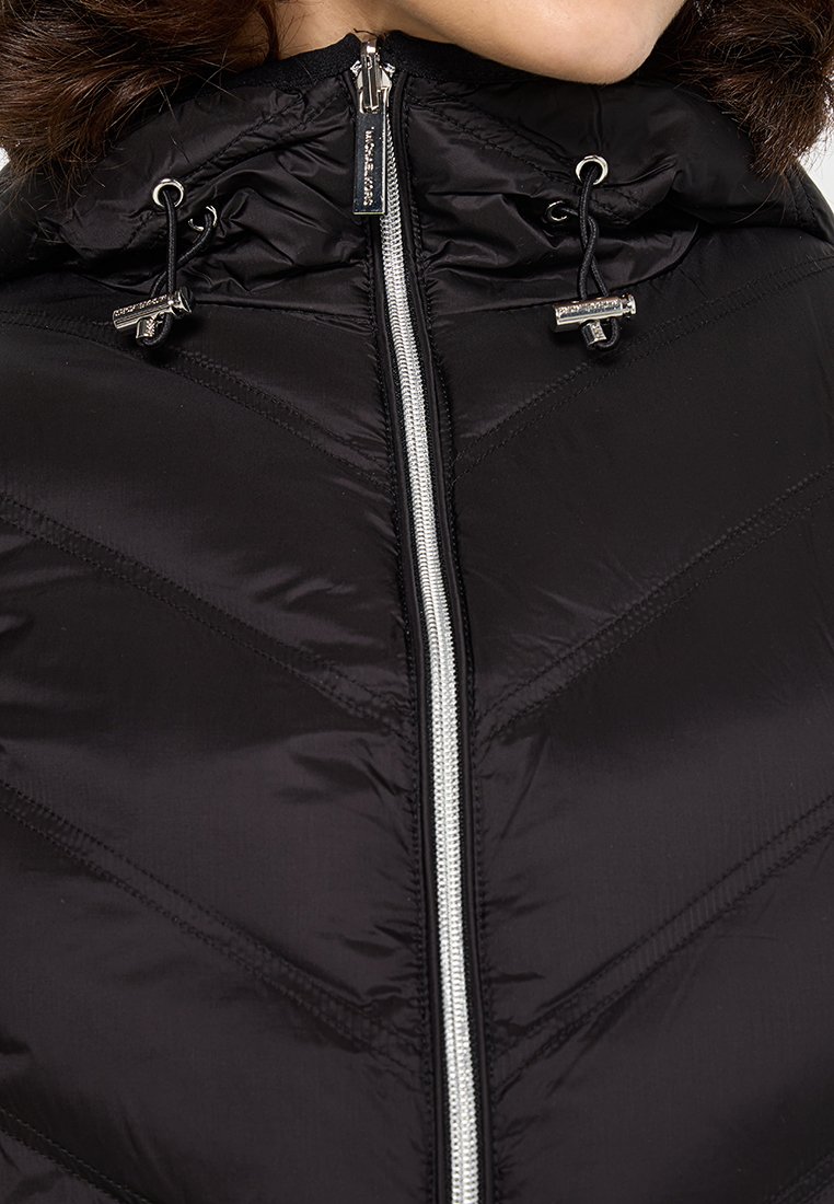 Veste matelassée noire avec capuche, fermeture éclair argentée contrastante et motif de surpiqûres en chevron. Le matériau est lisse et brillant.