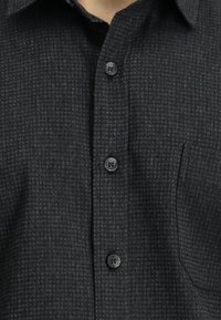 Czarna koszula zapinana na guziki z teksturowanym wzorem, posiadająca kołnierzyk, pięć guzików i pojedynczą kieszeń na piersi.
