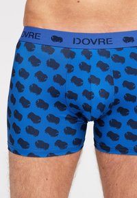 Blå boxershorts med et gentaget mønster af mørkeblå bisoner og en ensfarvet blå talje med brandnavnet "IDOVRE" i sort tekst.