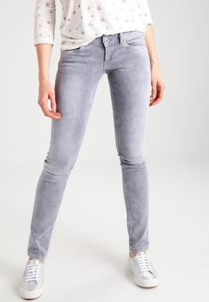 Osoba nosící světle šedé úzké džíny, bílé tenisky a bílé tričko s dlouhým rukávem s malými vzory hvězd.