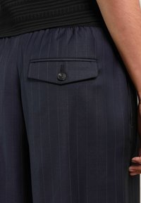 Marineblaue Hose mit einer Nadelstreifenmusterung, ausgestattet mit einer Gesäßtasche mit Knopf und einem elastischen Bund für zusätzlichen Komfort.