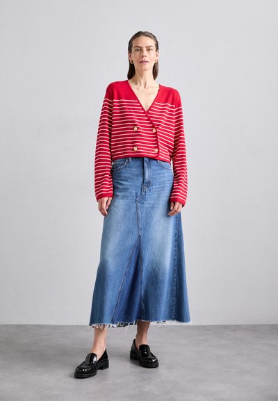Rood-witte gestreepte cropped cardigan met gouden knopen, gecombineerd met een lange blauwe denim rok met een split aan de voorkant en een franjezoom. Zwarte loafers.