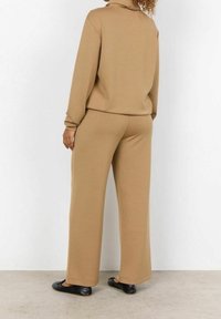 Beżowy sweatshirt i spodnie o szerokich nogawkach wykonane z miękkiego materiału. Strój cechuje wysoki dekolt i długie rękawy, w połączeniu z płaskimi czarnymi butami.