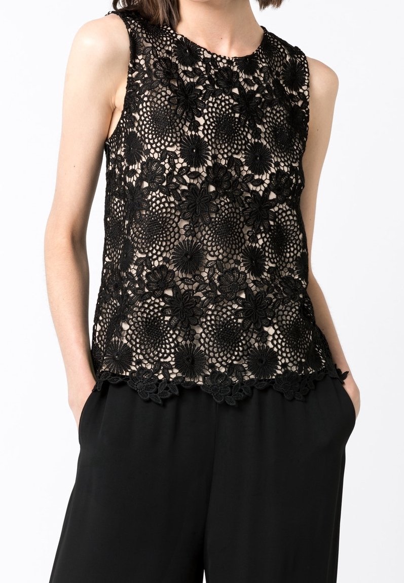Svart spets ärmlös topp med blomsterdesign, intrikata mönster, rundad halsringning och vågig nederkant, lagd över en beige bakgrund.