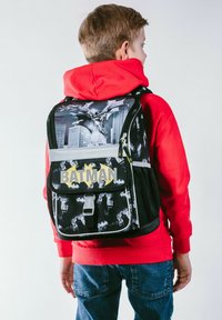 Zaino a tema Batman con design nero e grigio, caratterizzato da motivi di skyline, un logo giallo e una tasca con zipper frontale.