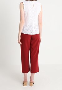 Bílý top s jemným vzorem a vlnitými rukávy, s klíčovou dírkou na zádech, spárovaný s červenými zkrácenými kalhotami a tanovými platformovými sandály.