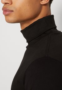Sort turtleneck med en jevn tekstur og figursydd design. Detaljert søm langs skuldrene, med høy krage.