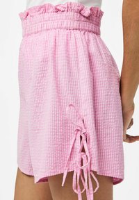Rožiniai gingham šortai su rauktiniu elastiniu juosmeniu ir šoninėmis juostelėmis. Audinys turi tekstūruotą, lengvą išvaizdą, užtikrinančią komfortą.
