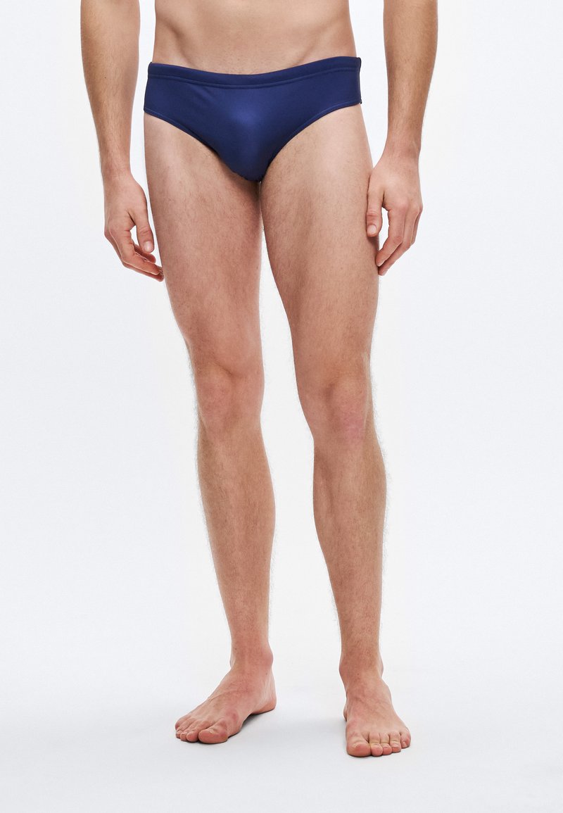 Cuecas de banho azul-marinho com textura suave, cintura baixa e cobertura mínima, concebidas para conforto e flexibilidade.