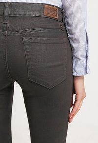 Jeans da uomo in denim grigio scuro con vestibilità slim, con tasche posteriori dal design triangolare e un'etichetta in pelle sul cinturino.