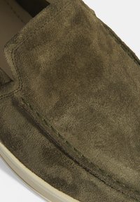 Grüne Wildleder-Slipper mit einer glatten Textur und kontrastierenden Nähten entlang der Kanten. Runde Zehenform und minimales Design.