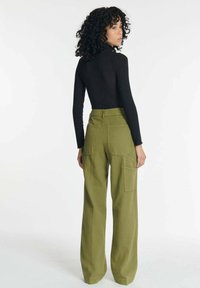 Strakke zwarte longsleeve top gecombineerd met hooggesneden olijfgroene wijde broek met zijzakken en een stevige stoftextuur.