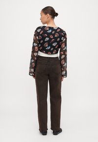 Blusa nera trasparente con un motivo di labbra colorate e conchiglie, abbinata a jeans dritti marroni a vita alta e scarpe nere.