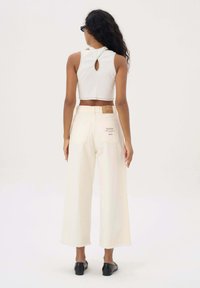 Witte cropped top met een keyhole rugontwerp, gecombineerd met hoge taille, wijde crèmekleurige broek en zwarte flats. Geleefde stoffen zichtbaar.