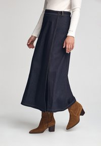 Lång mörk denimkjol med kontrastsömmar, en sidoflik och en framdragkedja. Kommer tillsammans med bruna mocka ankelstövlar och en åtsittande topp.