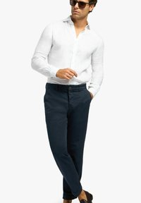 Witte lange mouwen linnen overhemd gecombineerd met donkergroene broek, zachte stoftextuur, op maat gemaakte pasvorm en bruine schoenen die de outfit aanvullen.