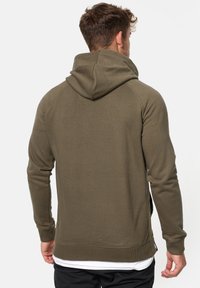Sudadera de color verde oliva con cuello alto y capucha. Presenta mangas raglán, puños y dobladillo de canalé, y una tela texturizada. Diseño simple y funcional.