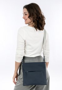Borsa a tracolla in pelle blu navy con una texture liscia, dotata di una tasca frontale con zip e una tracolla regolabile. Design rettangolare semplice.
