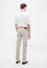 Gaiši pelēkas džinsa bikses ar šauru piegriezumu, piecām kabatām un brūnu ādas plāksteri aizmugurē. Valkātas kopā ar baltu T-kreklu un melniem apaviem.