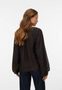 Blusa nera, trasparente, a maniche lunghe con una vestibilità comoda, caratterizzata da un tessuto testurizzato e un collo arrotondato, abbinata a pantaloni in denim blu scuro.