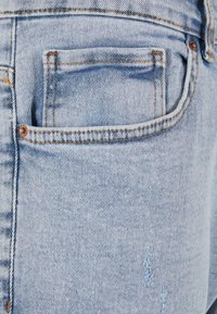 Jeans de mezclilla azul claro con un bolsillo trasero, que presentan costuras visibles y un ligero desgaste cerca de la zona del bolsillo.