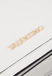 White textured leather handbag featuring a gold "VALENTINO" logo, black stitching, and a sleek, rectangular design.