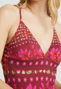 Red dress with floral patterns, featuring pink accents and thin straps. Fabric has a smooth texture with a fitted bodice and V-neck design.