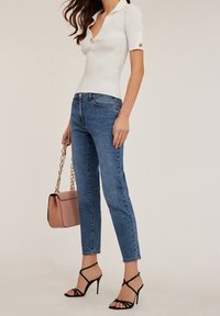 Biała prążkowana bluzka z krótkim rękawem, z kołnierzykiem i detalami guzików, w połączeniu z niebieskimi dżinsami o prostym kroju, czarnymi sandałkami na obcasie oraz różową torbą.