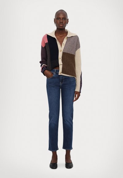 Cardigan de patchwork con botones, que presenta una mezcla de colores que incluye rosa, púrpura y beige, usado sobre jeans rectos azules.
