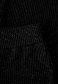 Mustast soonikust kangas, milles on peened metallikniidid, laiast elastse vöökohaga ja tekstuursete pindadega detailid.