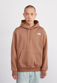 Sudadera de algodón marrón con un bolsillo delantero y capucha ajustable con cordón. Presenta un logo blanco en el lado izquierdo del pecho y puños acanalados.
