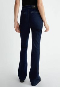 Tmavě modré rozšířené džíny vyrobené z denimu. Mají středně vysoký pas, dvě zadní kapsy a čistý lem.