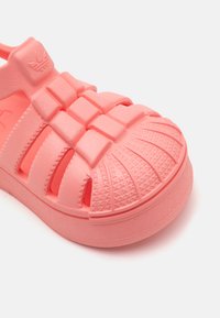 Sandal de borracha rosa com biqueira fechada, sola texturizada e design com fendas para ventilação. Apresenta um logótipo na tira e detalhes em relevo.