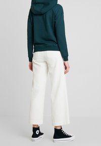 Sudadera con capucha de color teal, pantalones de pana blanca de corte holgado y zapatillas negras de caña alta. Diseño minimalista con puños acanalados y detalles de bolsillo.