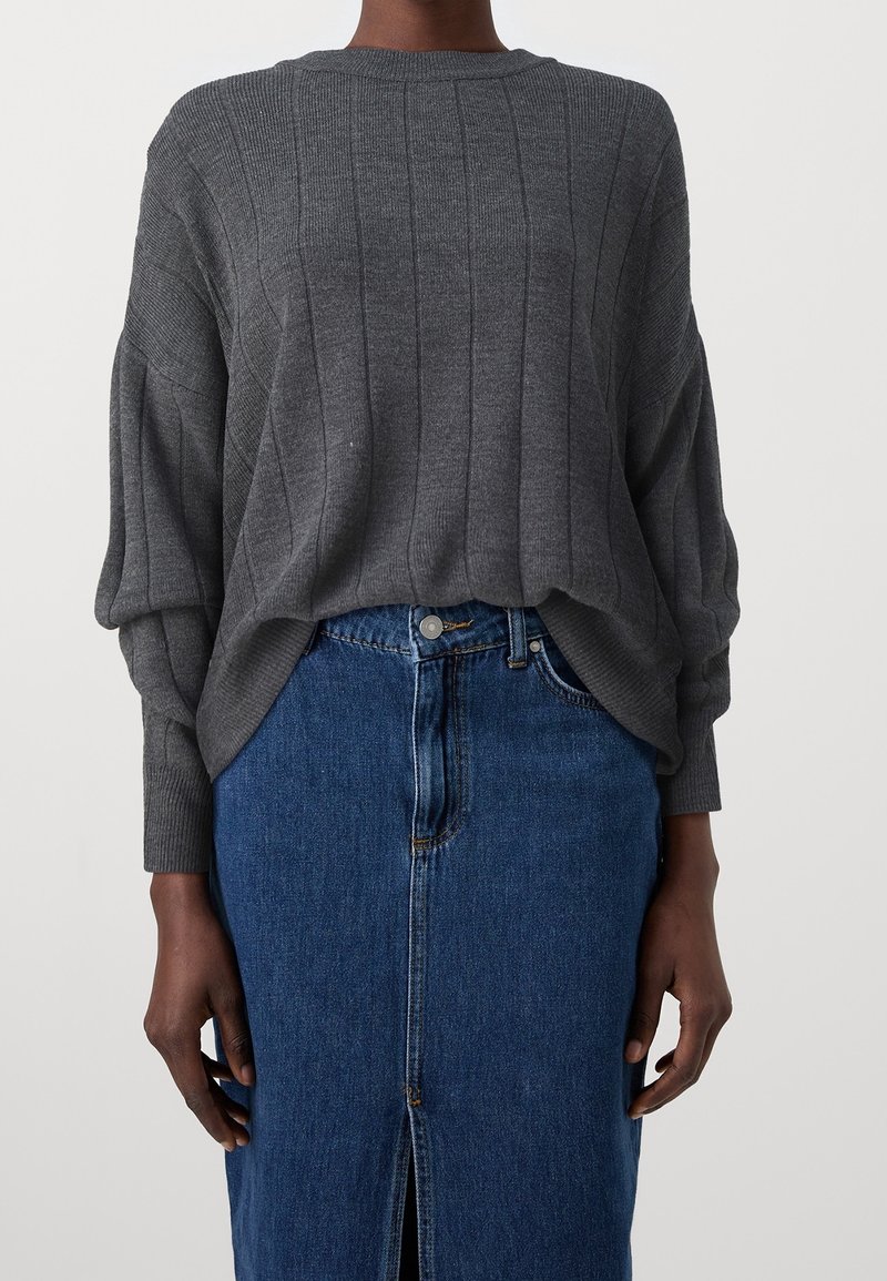 Maglione grigio a coste con scollatura rotonda e maniche lunghe e ampie, abbinato a una gonna di jeans blu con spacco frontale e chiusura a bottoni.