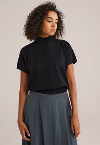 Top nero a maniche corte con collo alto, abbinato a una gonna fluida di un grigio chiaro. Tessuto morbido con un design semplice e minimalista.