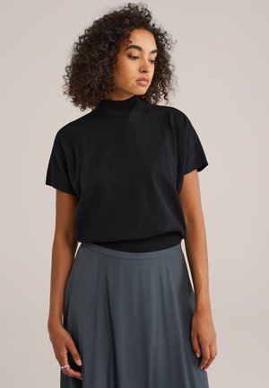 Haut noir à manches courtes avec un col haut, associé à une jupe fluide de couleur gris clair. Texture de tissu douce avec un design simple et minimaliste.