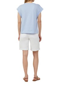 Jasnoniebieska bluzka z krótkim rękawem, białe szorty z podwiniętymi mankietami i brązowe sandały. Gładki materiał z luźnym krojem i subtelnym wzorem na ramionach.