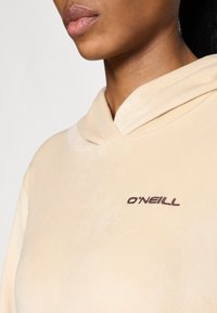 Beżowa bluza z kapturem o miękkiej teksturze, z kapturem i małym brązowym logo "O'Neill" wyszytym z przodu. Prosty design i kolor.