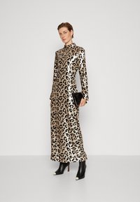 Mekko, jossa on leopardikuvio, pitkät hihat, korkea kaulus ja kiiltävää kultakangasta. Mustat nilkkurit, joissa on valkoiset varpaat. Musta käsilaukku.