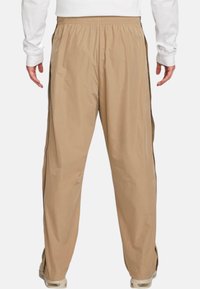 Beige träningsbyxor med siddragkedjor, elastisk midja och en slät textur, utformade för komfort och rörlighet.